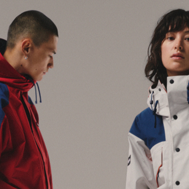 On the left- a man looking towards the floor wearing a red and blue jacket, on the right there is a woman looking at the camera wearing a white and blue coat